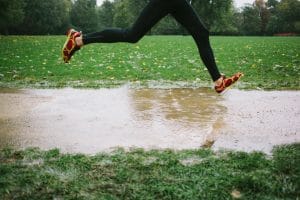 Photo of legs of a runner in the rain jumping over a puddle